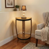 The Lamp Side Table, crafted from reclaimed whiskey barrels, features a lamp, small plant, and framed art next to a beige armchair with a knitted blanket.