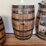 The Half Barrel Cabinet with Shelf - C002, priced at $450.00, repurposed into a cabinet with a small black latch and placed on a wooden floor near similar barrels exudes rustic charm and offers a unique storage solution.