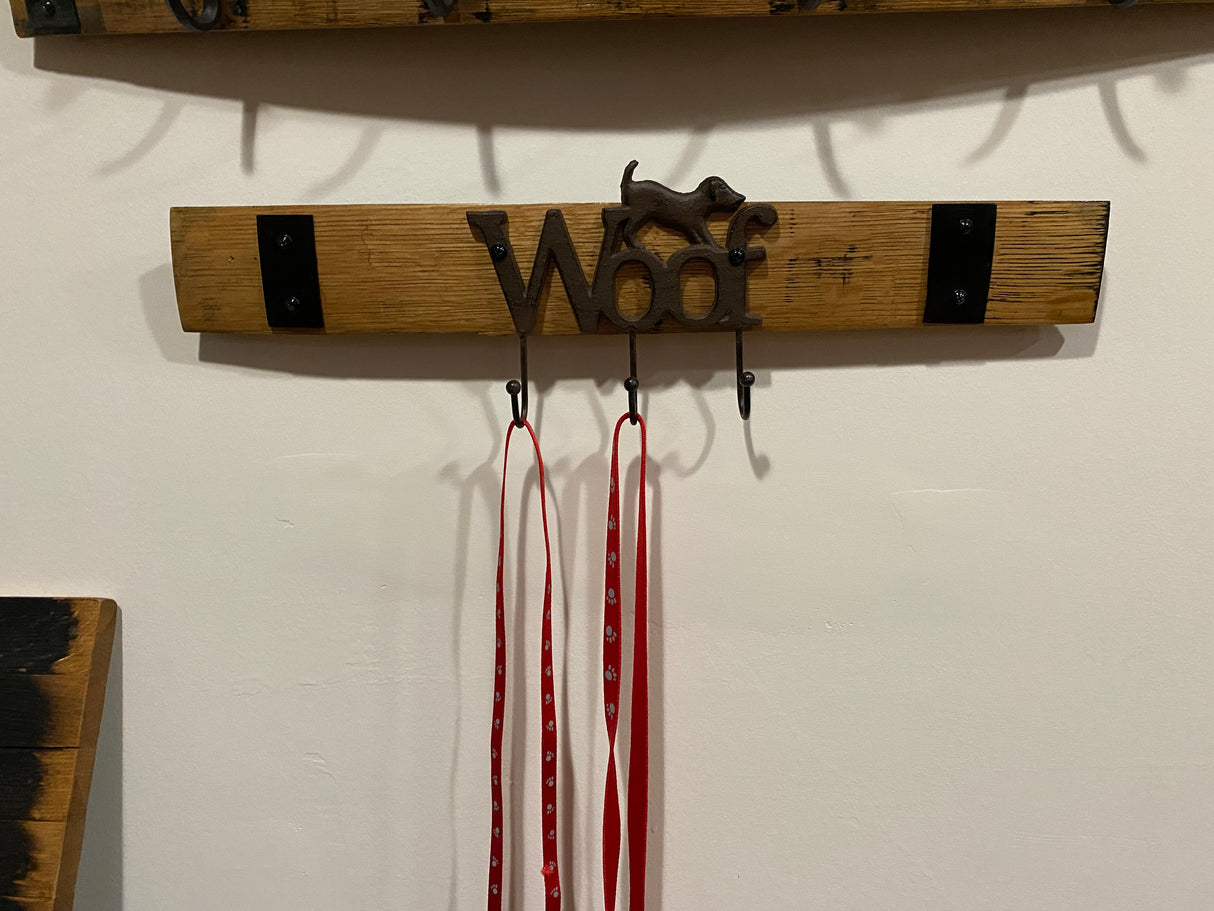 The Leash Holder, crafted from whiskey barrel staves with a playful "Woof" design, holds three red and white leashes. Perfect for home decor, it adds a rustic touch to your entryway.