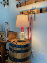 The Maker's Mark Lamp, fashioned from a bottle and set on a whiskey barrel, exudes rustic charm. It pairs beautifully with the wooden wall hooks featuring a "Woof" sign in the background.