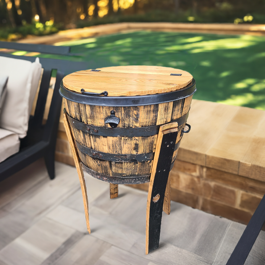 A hand-made solid wood barrel Outdoor Bottle Cooler, crafted to fit whiskey, wine, and beer bottles, stands on three legs near a patio and green lawn.