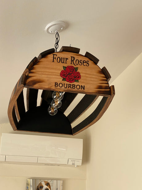 Upcycled bourbon barrel pool table light with "Four Roses" custom logo, hanging from the ceiling. Dog picture on wall below.