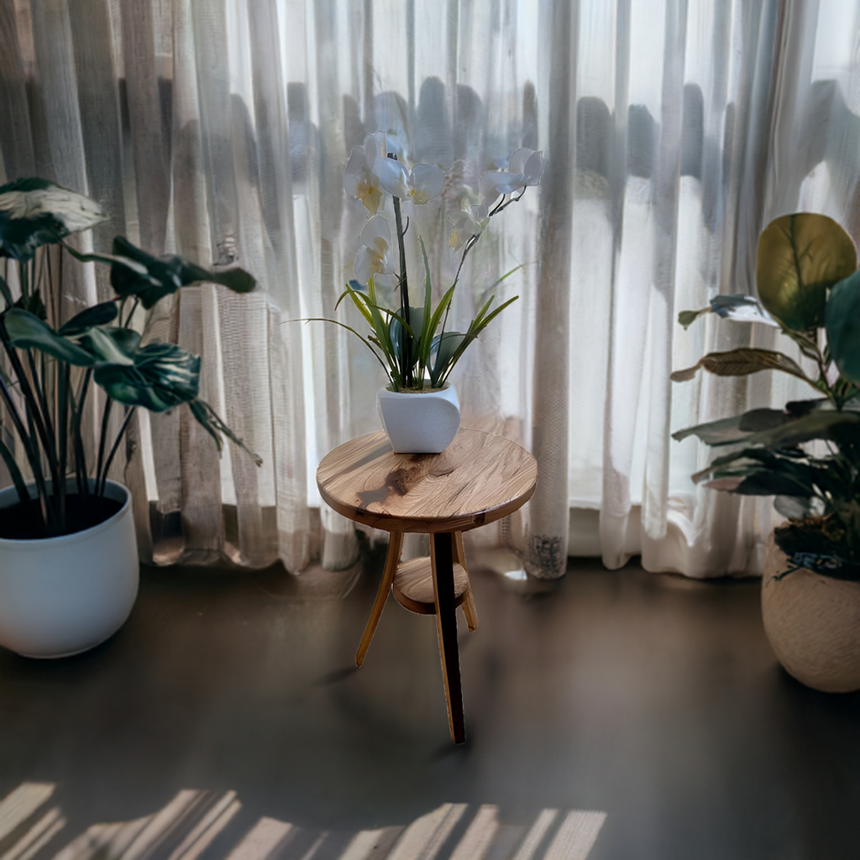 A white orchid in a pot sits on a Stave Whiskey Barrel Plant Stand atop a wooden table, surrounded by plants near sheer curtains in sunlight.