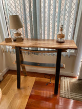 Stave Sofa table with a Burnt Hickory Top, a lamp, and decor items, along with a shelf underneath. Placed in front of vertical blinds by the window. Accessories not included. Priced at $325.00.
