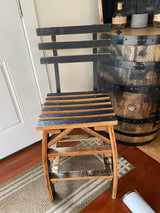 A rustic Whiskey Barrel Stave Chair with Back, priced at $250.00, sits next to a wooden barrel inside a room with hardwood floors and a rug.