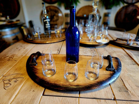 A rustic Wine Tasting Tray with handles holds a blue bottle and five empty glasses, all set on a vintage table for an elegant wine tasting experience.