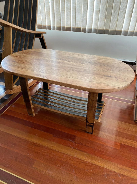 Whiskey Barrel Stave Oval Coffee Table with a stave shelf, placed on a wooden floor near a window with vertical blinds, priced at $350.