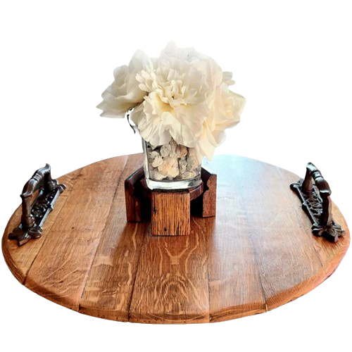 The hand-crafted Charcuterie and Cheese Round Wooden Serving Board, featuring a natural wood finish, exudes rustic charm with two handles. Topped with a glass vase of white flowers, it beautifully echoes the essence of a whiskey barrel charcuterie.