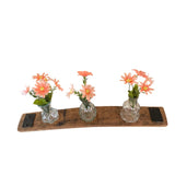 A Bud Vase Stand featuring three small glass vases with pink flowers sits gracefully on a rustic barrel stave, exuding charming elegance.